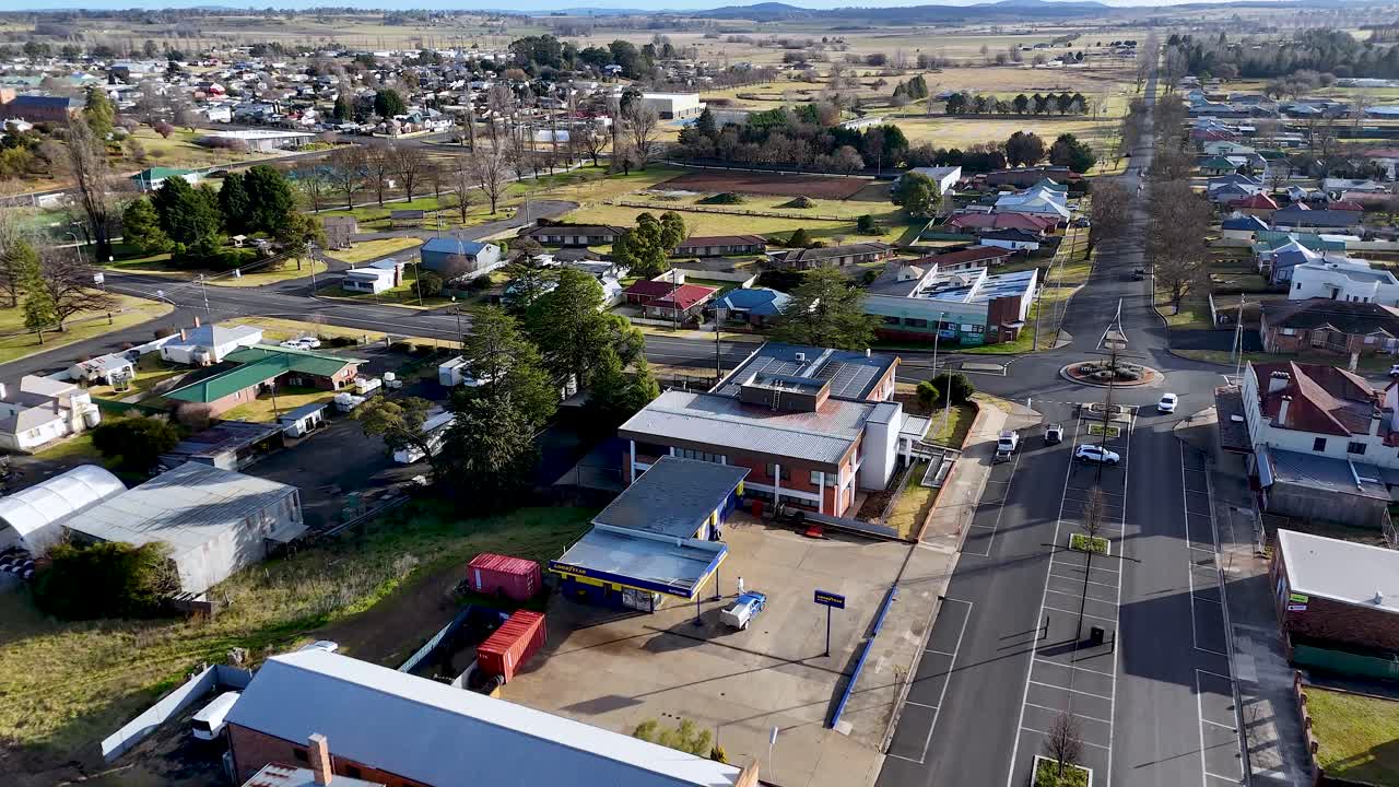Drone footage moves above a quiet city junction in Glen Innes, Australia, showing commercial buildings, residential homes, and clear winter daylight with steady camera motion