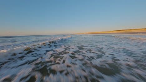 spectacular fpv drone shot flying closely over breaking waves at very high speed during sunset