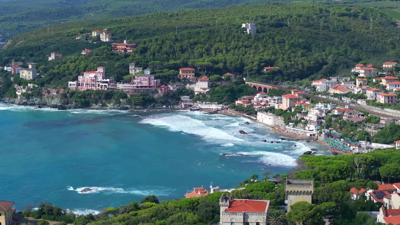 Ripresa aerea laterale che mostra splendide onde lunghe che si riversano nella riviera balneare di Castiglioncello, Italia.