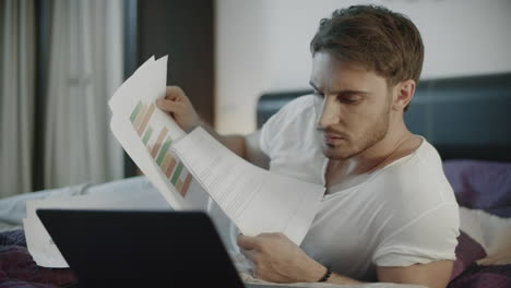 serious man working with documents and laptop on sofa at night