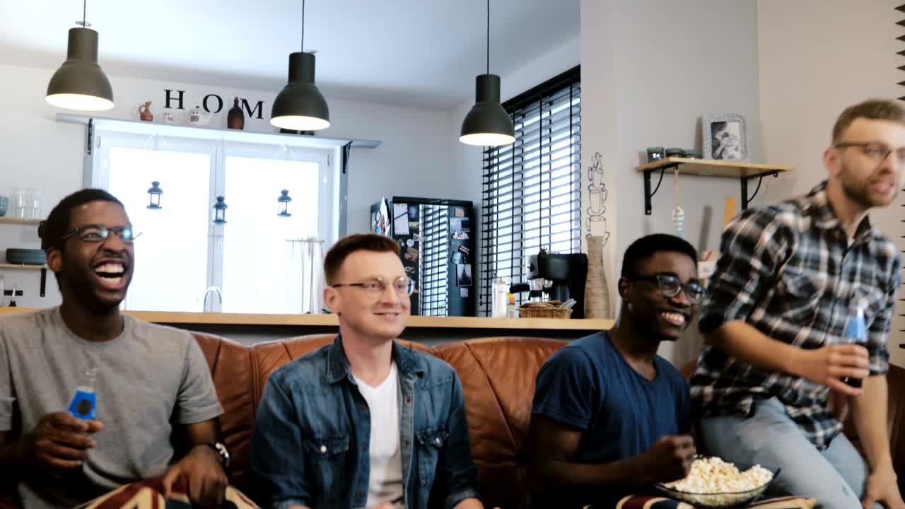 Følelse. Afroamerikanske menn ser sport på TV 4K. Nerdy fotballfans av blandet rase feirer mål på sofaen med popcorn