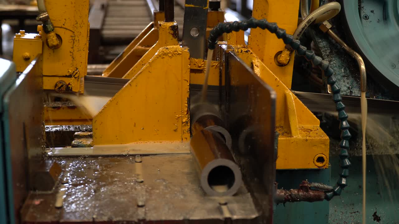 Industrial band saw, cutting metal pipe, coolant in yellow scene, industrial tools