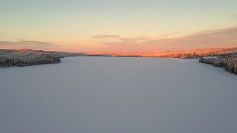 aerial view of sunset over snowy frozen lake in deep forest with hills and mountains