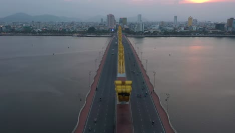 drone rising above dragon bridge cau rong, traffic and city skyline during sunset in danang, vietnam