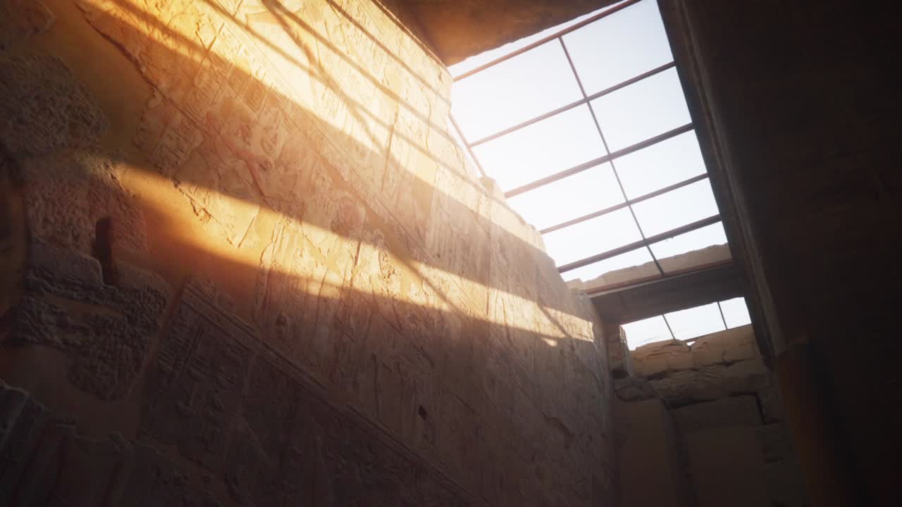 Light streaks shining on a wall with hieroglyphs through a roof window inside the Kamak Temple in Luxor, Egypt. 
Slow camera rotation