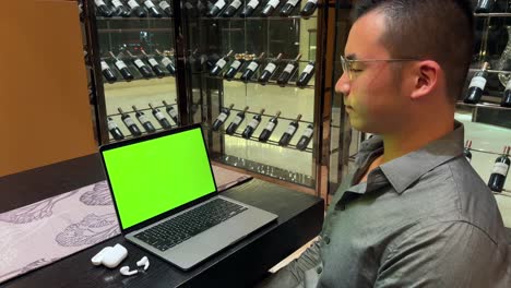 empresario masculino asiático mirando una computadora portátil con pantalla verde en una casa de lujo con una amplia pantalla de vino