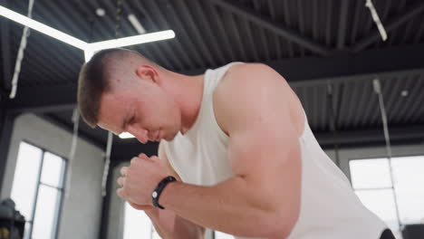 close up view of fitness enthusiast performing warm up exercise with hands clasped at chest level and head bowed wearing strap in bright studio emphasizing concentration muscle activation