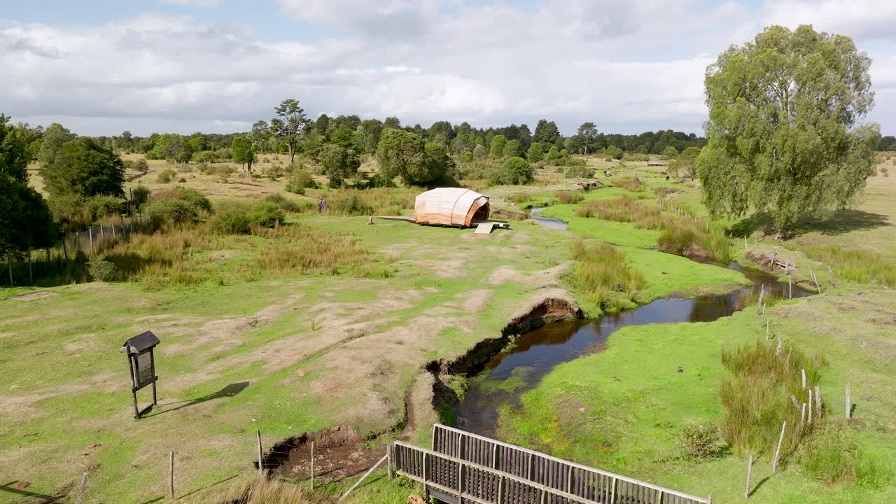 Low altitude drone shot of the Monte Verde archaeological site, showing the landscape, the stream, and a replica hut in Puerto Montt, Chile