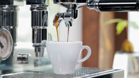 close up of white espresso cup, pouring over delicious golden brown coffee extracted from tasty coffee beans in espresso machine