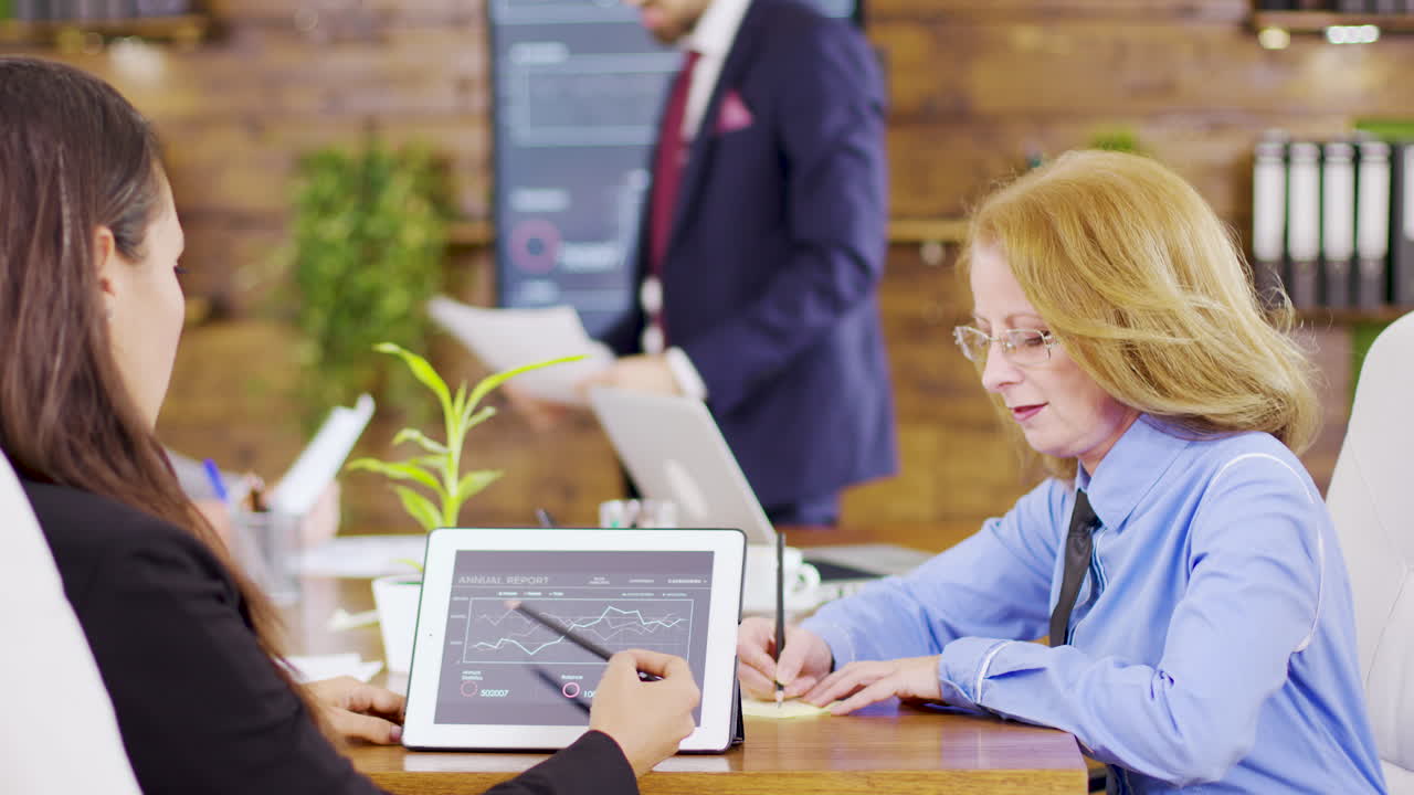 Female colleagues analysing charts on tablet in the meeting room