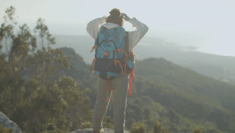 Vista-Trasera-De-Una-Excursionista-Parada-En-La-Cima-De-La-Montaña-Con-Las-Manos-Arriba-Y-Disfrutando-De-La-Vista