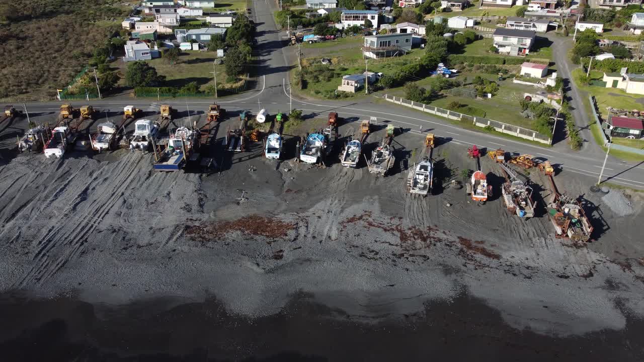 volando a lo largo de una línea de barcos estacionados en una playa en ngawi, nueva zelanda