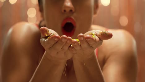 young woman blowing golden glitter to camera