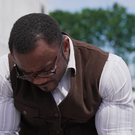 Serious black skinned man looking into phone. Portrait of african american guy with muscular body in suit sitting outdoors and using mobile phone