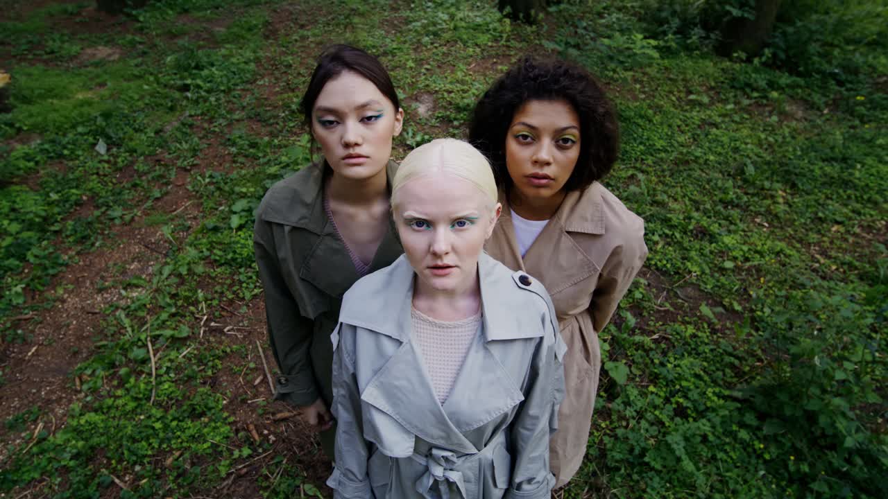 Three women in trench coats in a forest