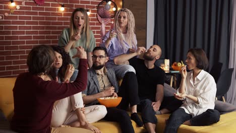 Friends-eating-popcorn-from-a-bowl-while-sitting-on-a-sofa-and-talking