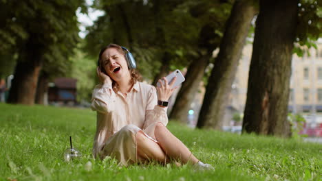 mujer joven feliz con auriculares inalámbricos eligiendo, escuchando música en el teléfono inteligente bailando al aire libre