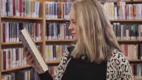 Caucasian-female-girl-picked-up-black-english-book-from-a-shelf-in-library,-side-shot-of-her-face