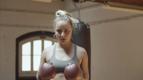 Front-view-of-female-boxer-in-boxing-gloves-standing-in-gym