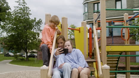 una niña con síndrome de down y sus amigos haciendo una selfie con un teléfono inteligente en el parque en un día ventoso