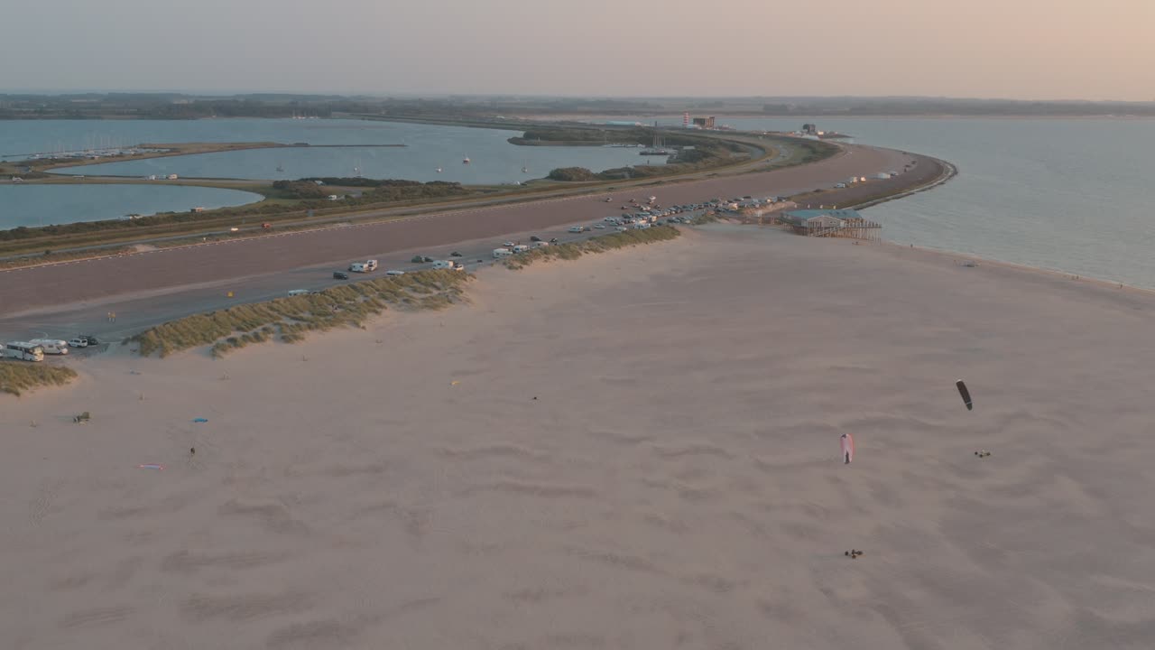 drone cinemático - toma aérea de la playa natural verde y arenosa al atardecer con turistas y personas con buggykiting en zelanda en el mar del norte, países bajos, 30p