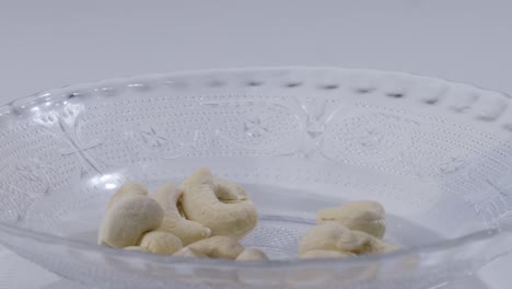 close up static shot of cashew nuts falling into empty plate on table