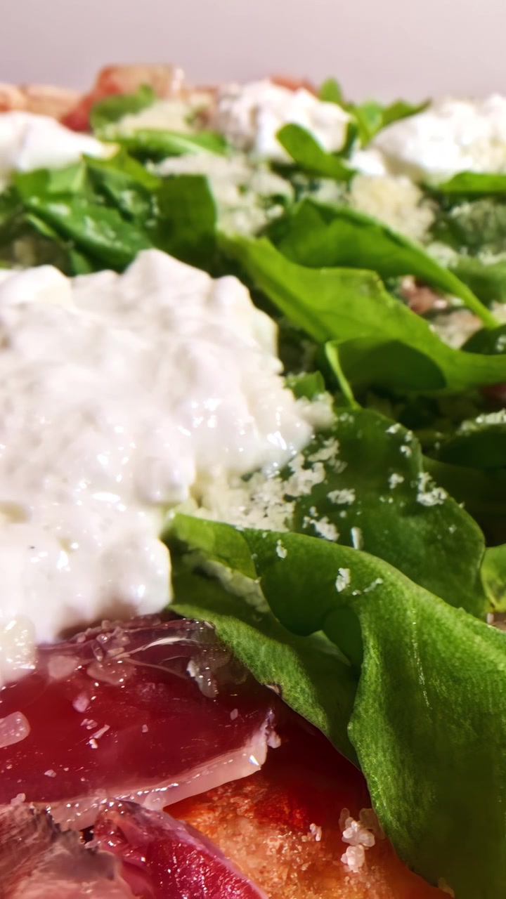 Un primo piano di cremosa burrata che si scioglie su una vivace pizza con rucola e prosciutto, catturando l'essenza della cucina italiana.