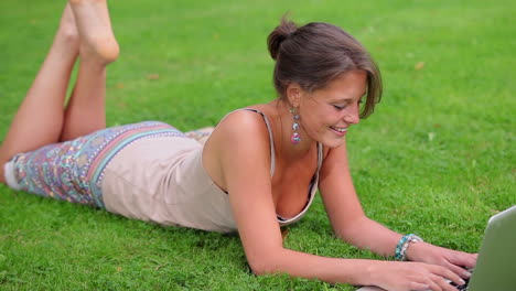 Happy-student-lying-on-grass-using-her-laptop