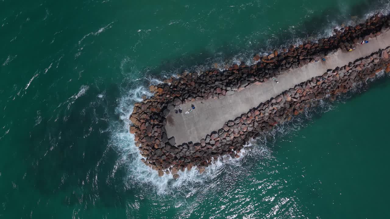 Drone top down of crashing surf at breakwall tip off Blacksmiths Beach, midday light, NSW Australia