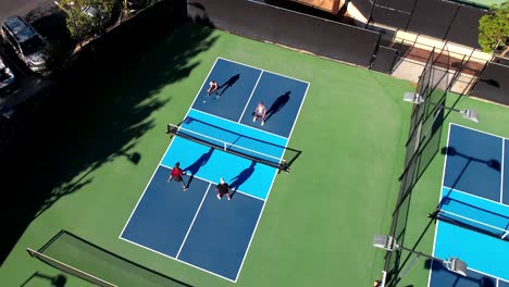 pickleball match on blue outside court, foursome playing the sport, drone rising over players