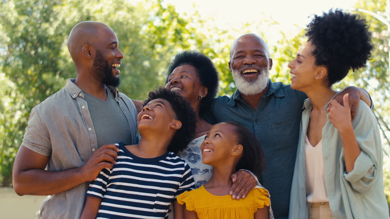 Portræt af en multigenerationsfamilie, der står udendørs i en have eller på landet og smiler til kameraet.
