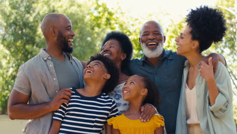 Retrato-De-Una-Familia-Multigeneracional-Parada-Al-Aire-Libre-En-El-Jardín-O-En-El-Campo-Sonriendo-A-La-Cámara