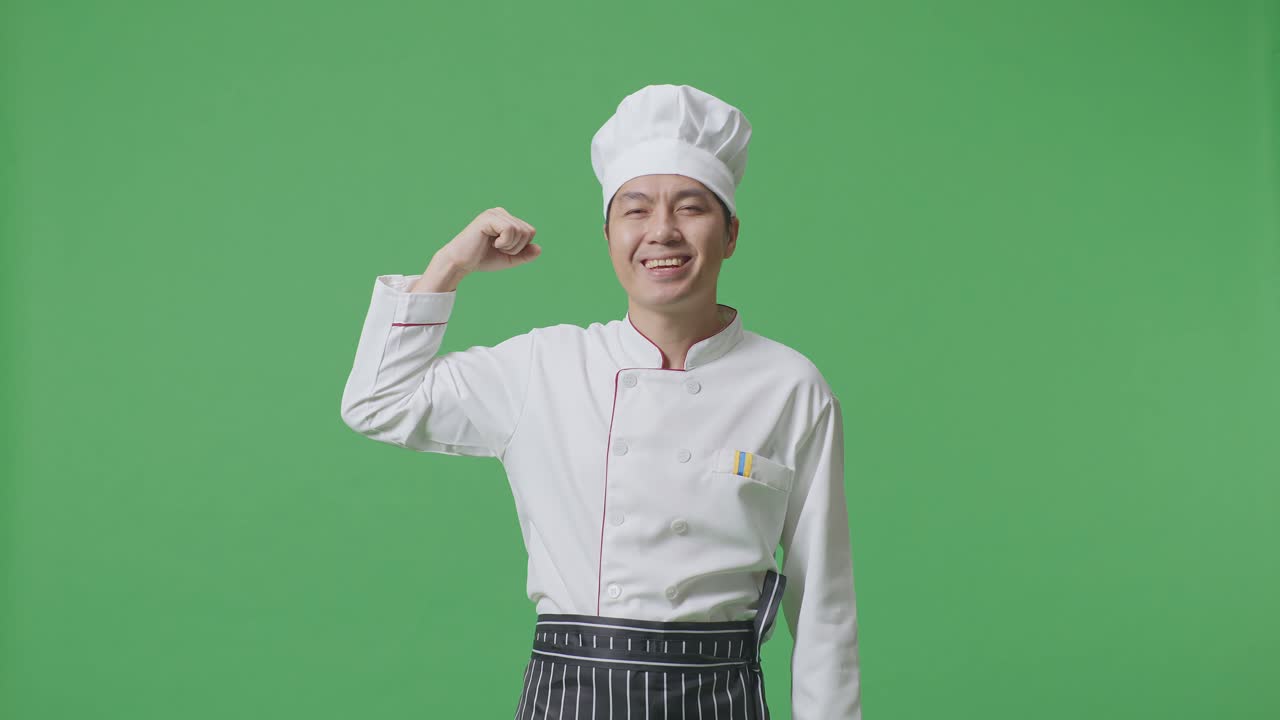 el chef asiático sonriendo y flexionando su bíceps mientras está de pie en el estudio de fondo de la pantalla verde
