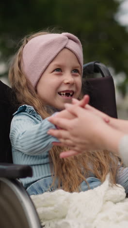 toothless girl laughs while playing fun game with mother in spring park. woman enjoys entertaining little daughter with injury in wheelchair closeup