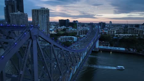 Drone-pull-away-close-up-shot-of-Story-Bridge,-camera-narrowly-passes-top-of-bridge,-pans-down-revealing-bridge-structure-and-traffic-below