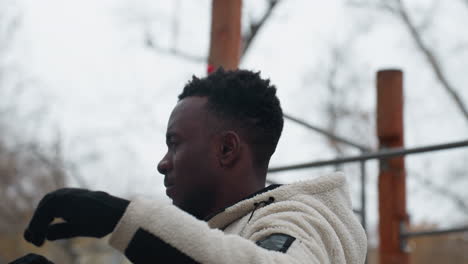 close-up of young man working out outdoors during winter, performing fitness exercise in front of wooden workout equipment, while pushing through the cold environment