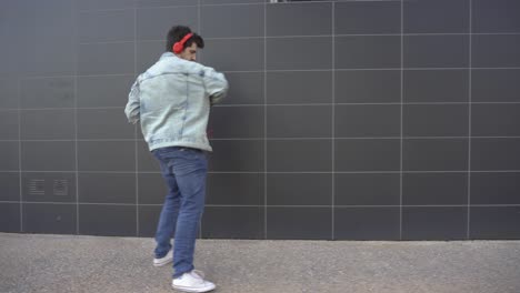 man dancing while walking down the street, listening to music through a phone and red headphones