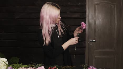 una joven florista limpia una flor de clavel rosa. variedad de flores. fondo oscuro