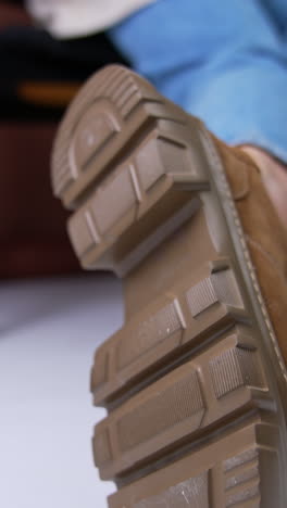 beautiful brown stylish suede shoes on massive tractor soles. model sitting on chair demonstrating her fashionable boots. close up. blurred backdrop. vertical video