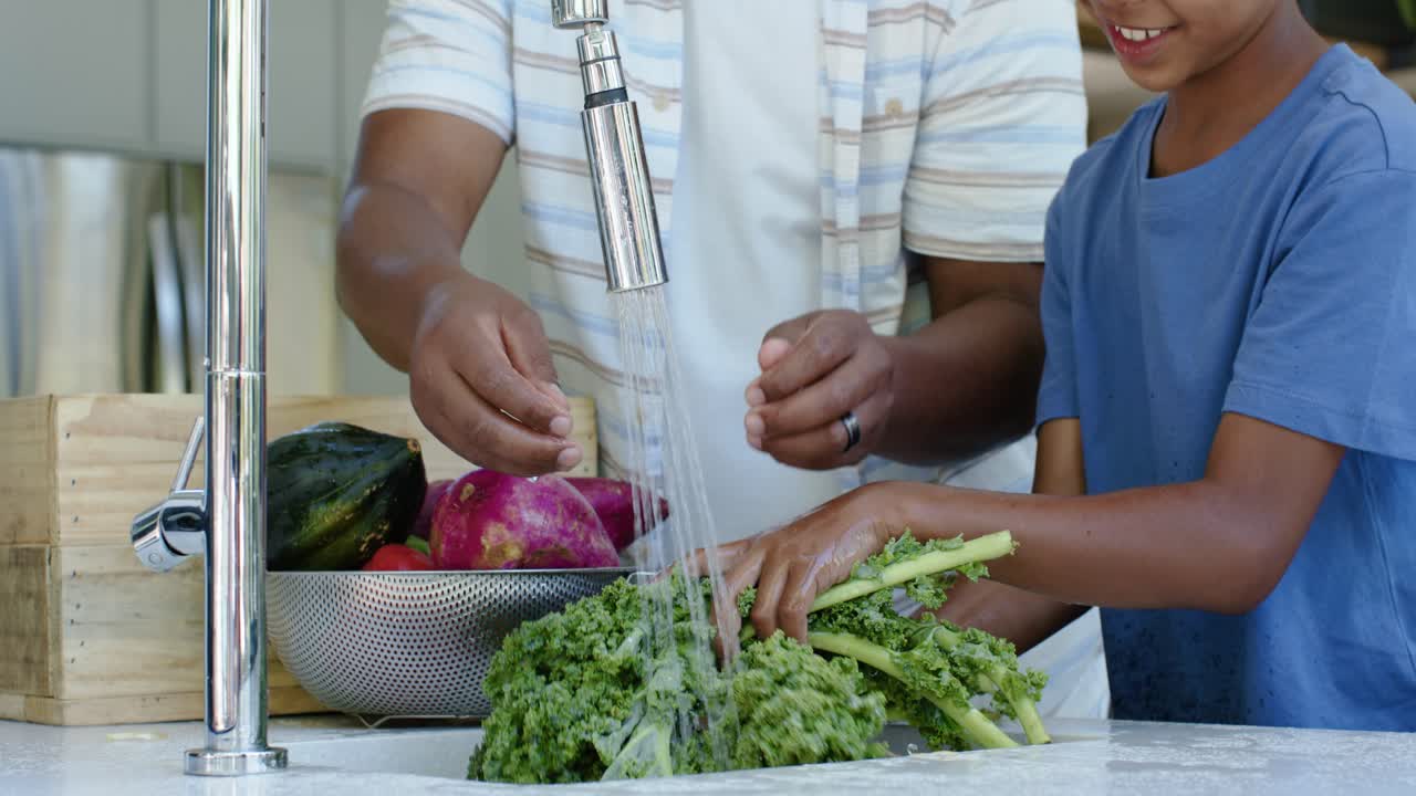 Père et fils afro-américains ouvrant le robinet, tenant du chou frisé et le rinçant à l'évier de la cuisine.