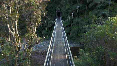 a drone shot taken passing through a swing bridge near rivendell in new zealand