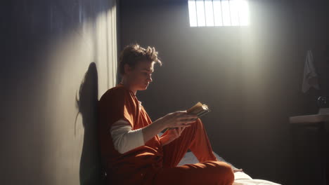 female inmate reading book alone on bed in sunlit prison cell