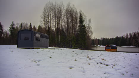 Cold-Winter-Morning-By-The-Lake-Shore-With-Wooden-Cabins,-Snow-Melting-On-A-Sunny-Day