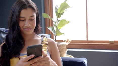 Happy-biracial-teenage-girl-relaxing-on-couch-using-smartphone,-smiling,-copy-space,-slow-motion