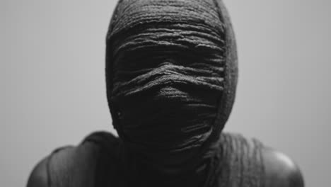 a mummy of a woman on a white backdrop rises her head