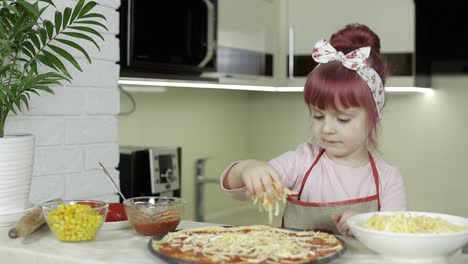 Pizza-Kochen.-Kleines-Kind-In-Schürze-Gibt-Geriebenen-Käse-Zum-Teig-In-Der-Küche