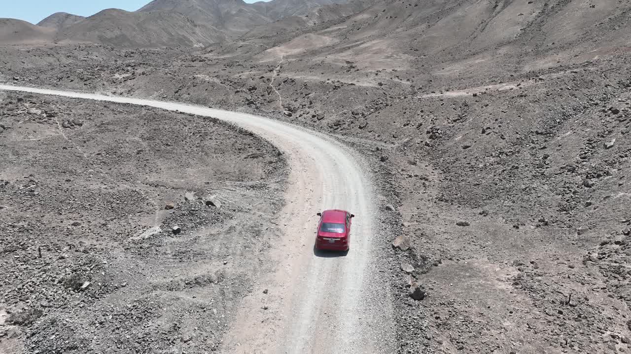 panorámica aérea y toma de carro de un vehículo rojo en movimiento lento en el desierto de perú a lo largo de un camino desértico polvoriento y seco en el páramo fuera de la ciudad santa de caral en un día soleado