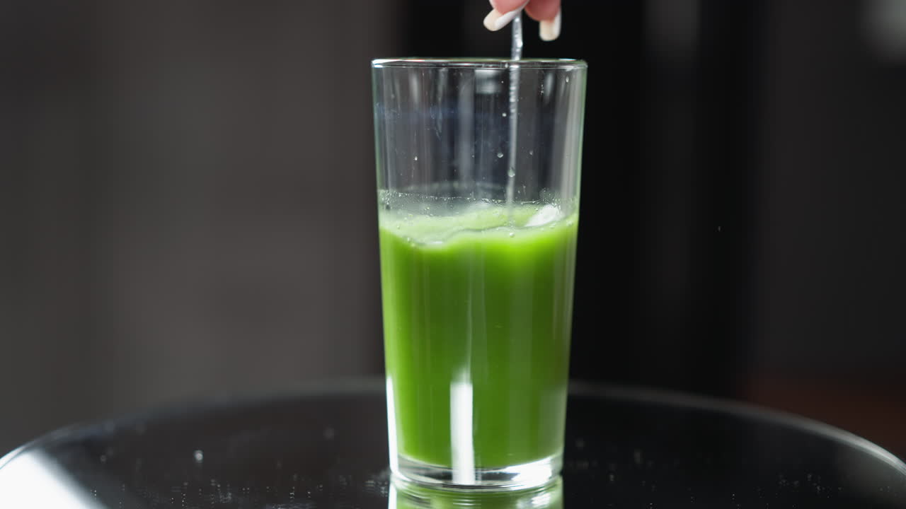 primer plano de una cuchara mezclando jugo de verduras verde vibrante en un vaso alto transparente, mezclando un jugo verde fresco con una cuchara en un vidrio alto, iluminación natural