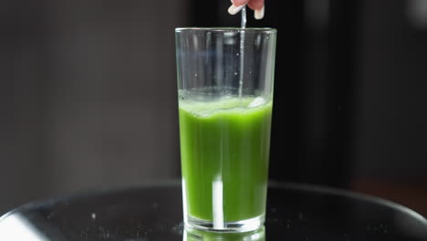 close-up of a spoon stirring vibrant green vegetable juice in a clear tall glass,stirring a fresh green juice with a spoon in a tall glass, natural lighting