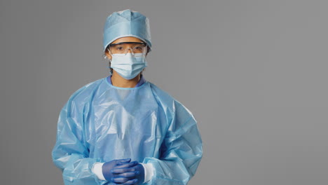 portrait of serious female surgeon wearing safety glasses and face mask against grey background